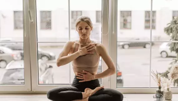 Femme pratiquant un exercice de respiration en tailleur, mains sur la poitrine et le ventre