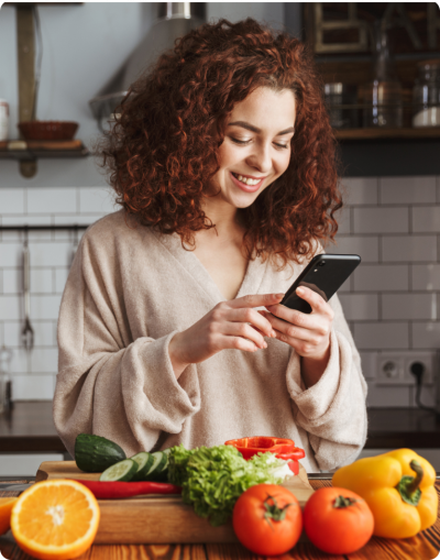 stock-photo-photo-of-joyful-caucasian-woman-holding-smartphone-while-cooking-salad-with-fresh-vegetables-in-1402613849 1.png